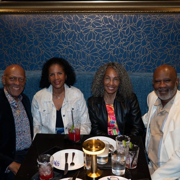 Four smiling people, two men and two women, seated at a restaurant table with drinks.