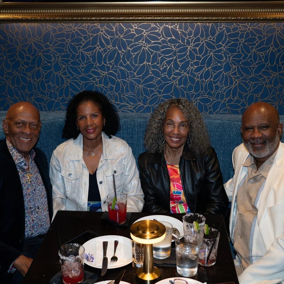 Four smiling people, two men and two women, seated at a restaurant table with drinks.