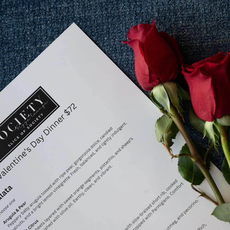 A Valentine's Day Dinner menu from Society Pizza Lounge, with two red roses on a blue textured surface.