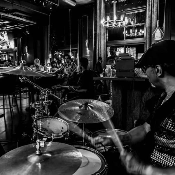 Black and white image of a drummer performing live music in a dimly lit bar.