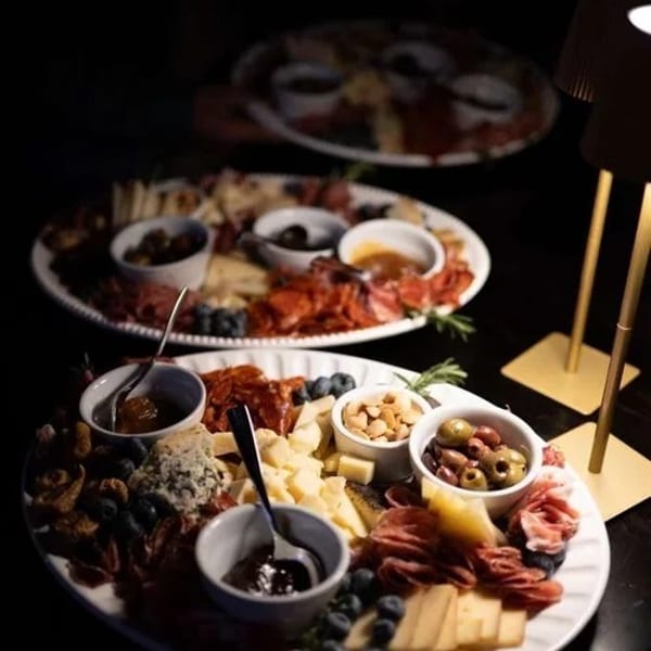 Three charcuterie boards with meats, cheeses, fruits, nuts, and olives under dim lighting.