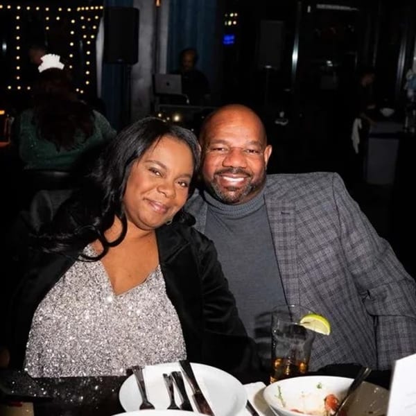 A smiling couple sits at a dark restaurant table with partially eaten food and drinks.