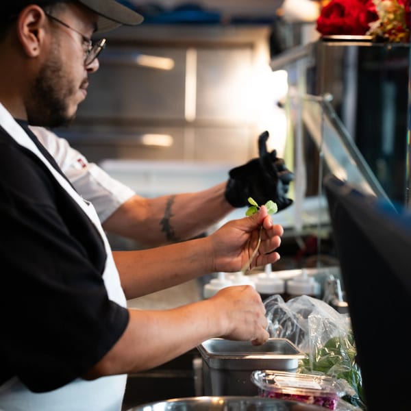 Two chefs in a commercial kitchen preparing food, one holding fresh herbs.