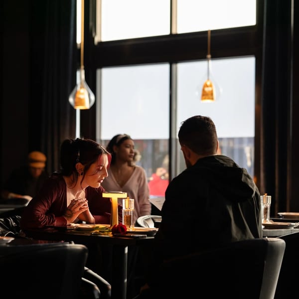 A couple sits at a dimly lit restaurant table, with another woman in the background.