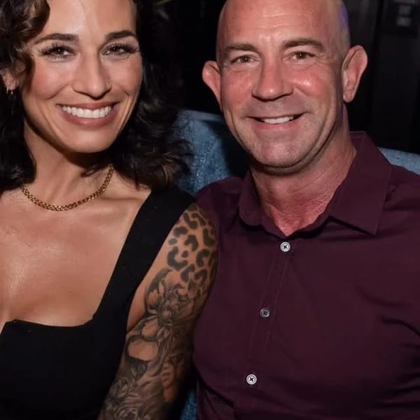 Smiling woman with tattooed arm and man in a maroon shirt sitting together in a dimly lit restaurant.