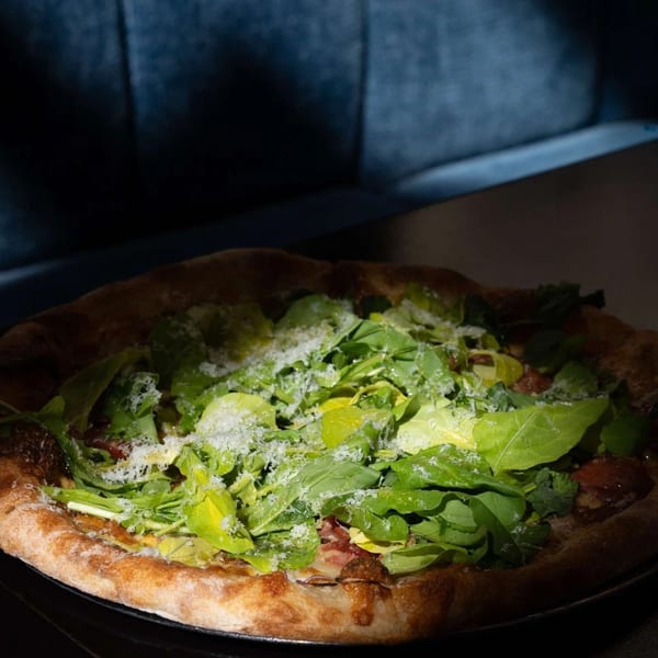 A freshly baked pizza topped with green arugula and grated cheese on a dark table.