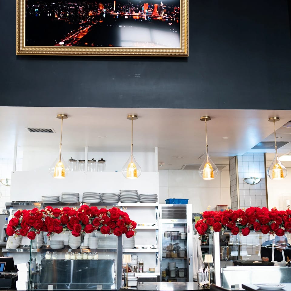 A restaurant interior with a framed cityscape above a counter adorned with red roses and pendant lights.